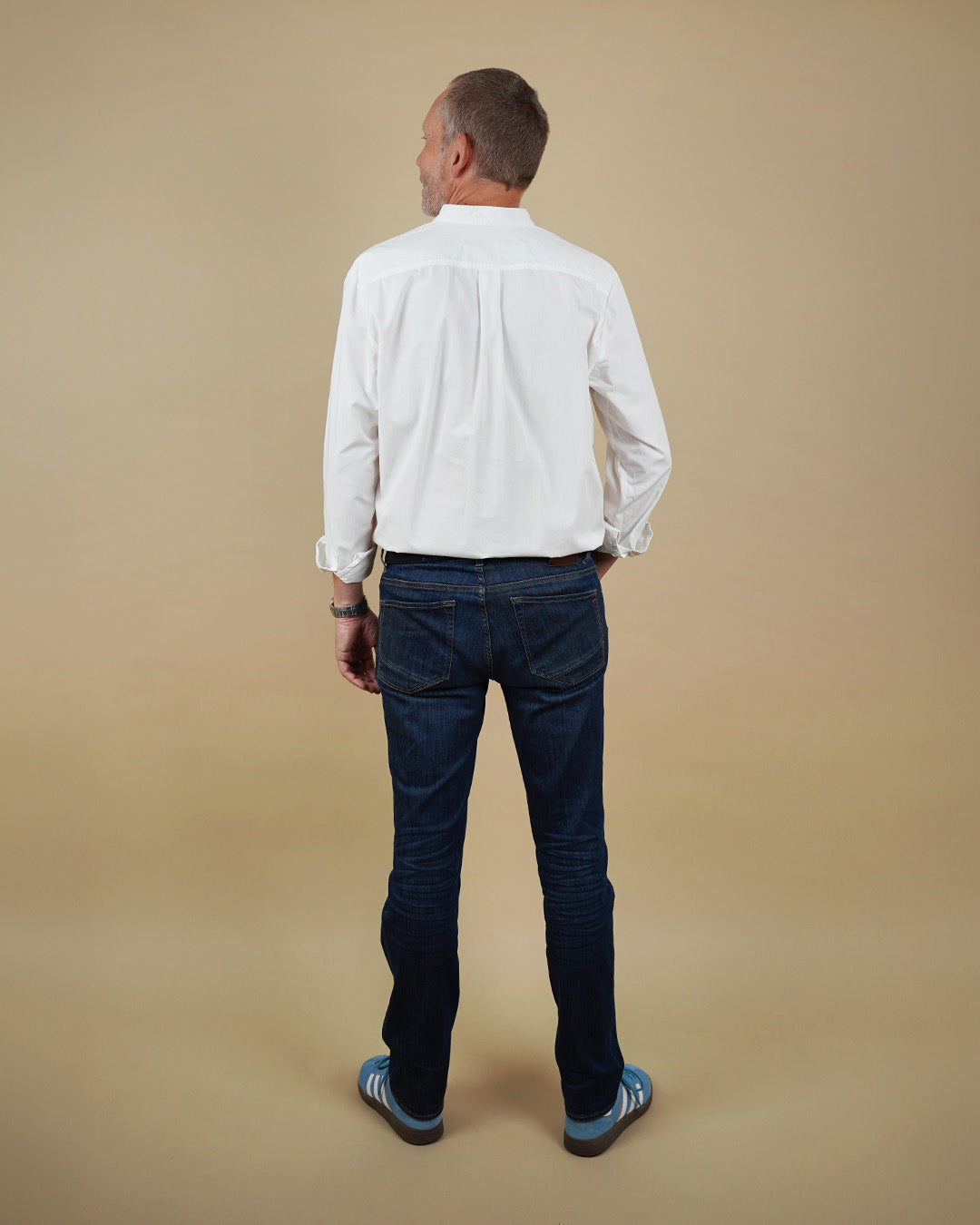 Man wearing a white shirt and dark jeans standing against a beige background