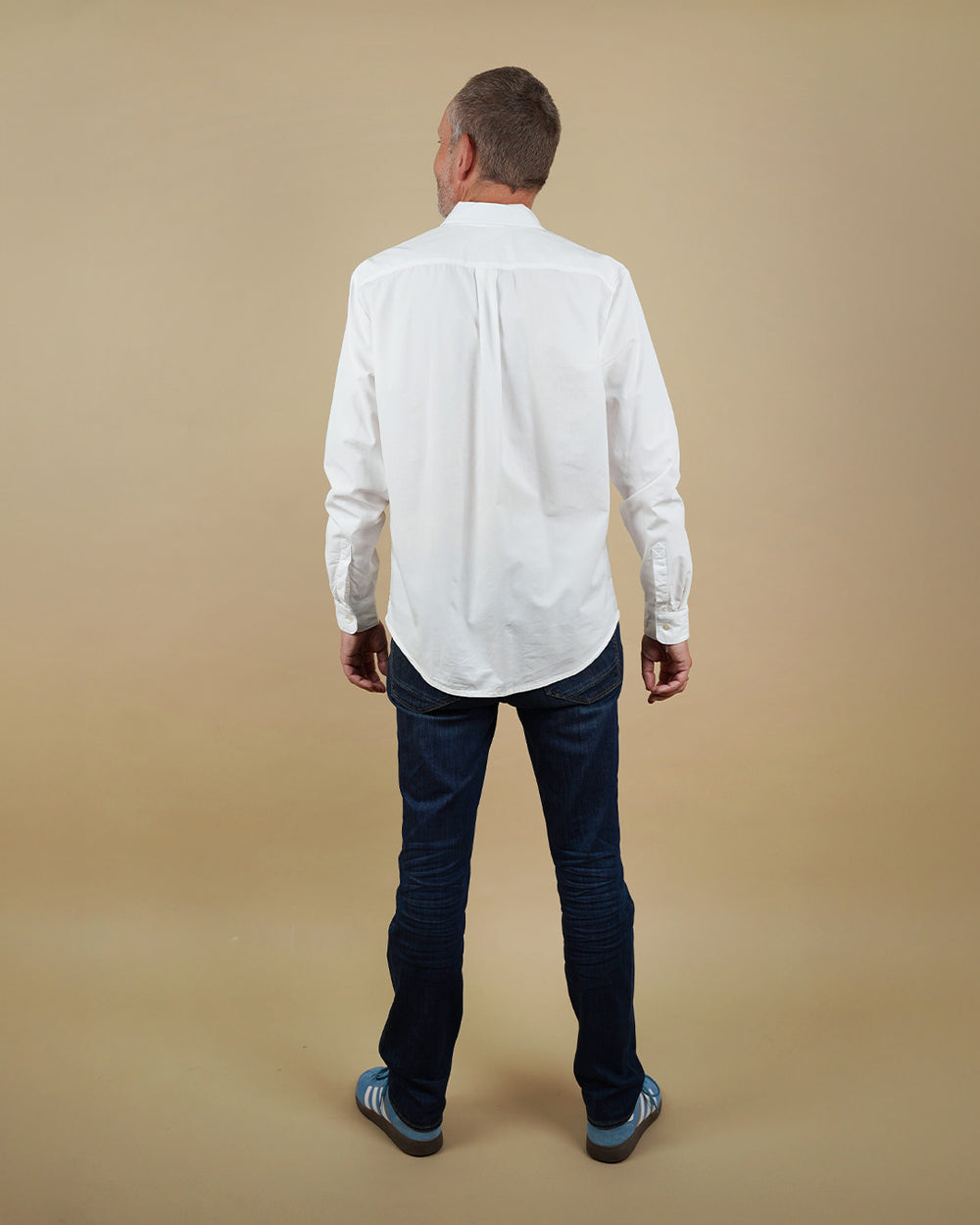 Man wearing a white shirt and dark jeans on a beige background