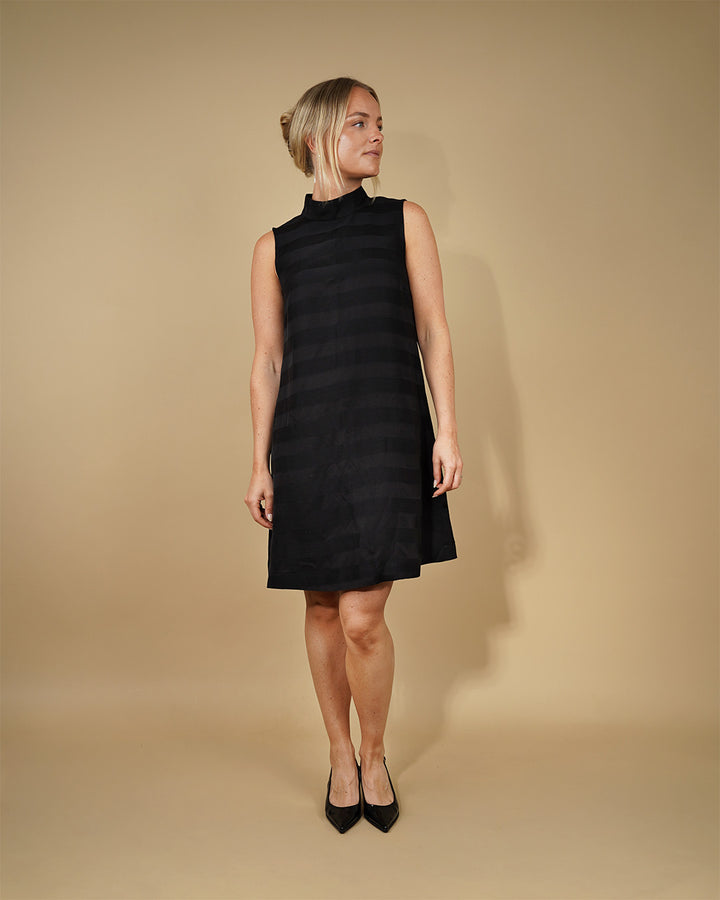 Woman wearing a black sleeveless dress against a beige background