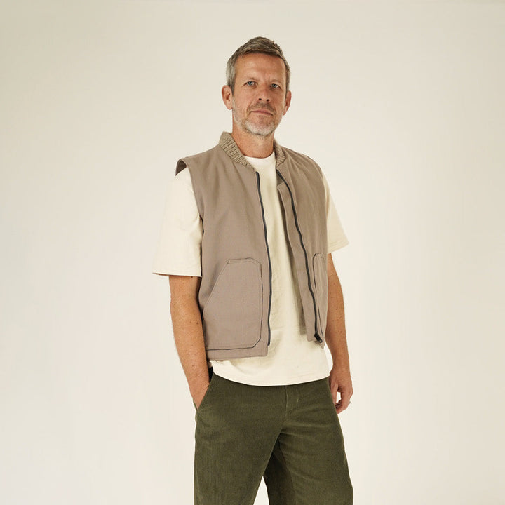 Man wearing a beige vest and green pants on a white background