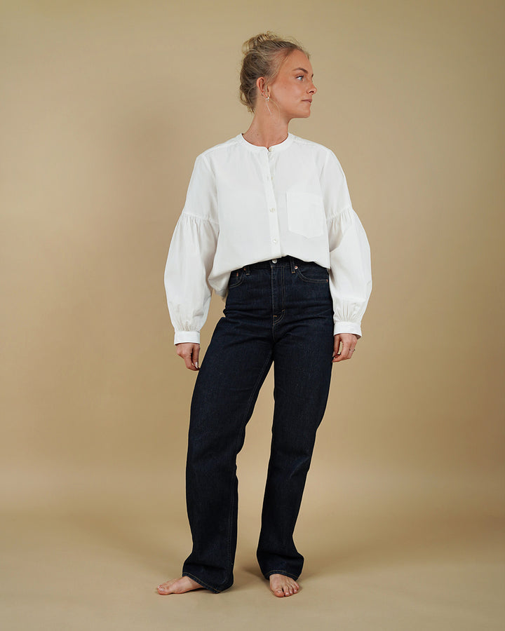 Person wearing a white blouse and black pants on a beige background