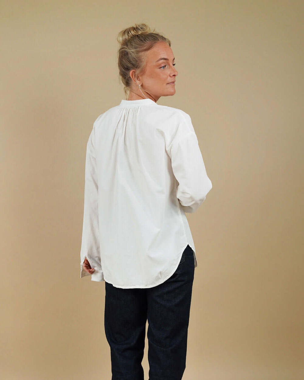 Person wearing a white blouse and dark pants against a beige background