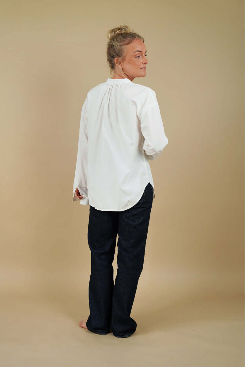 Person wearing a white blouse and dark pants against a beige background