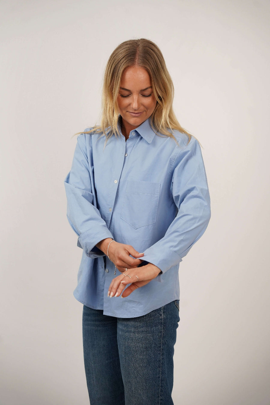 Woman wearing a light blue shirt and jeans on a plain background