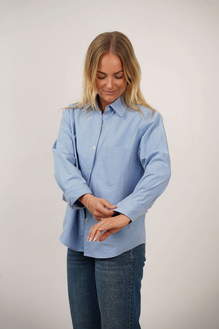 Woman wearing a light blue shirt and jeans on a plain background