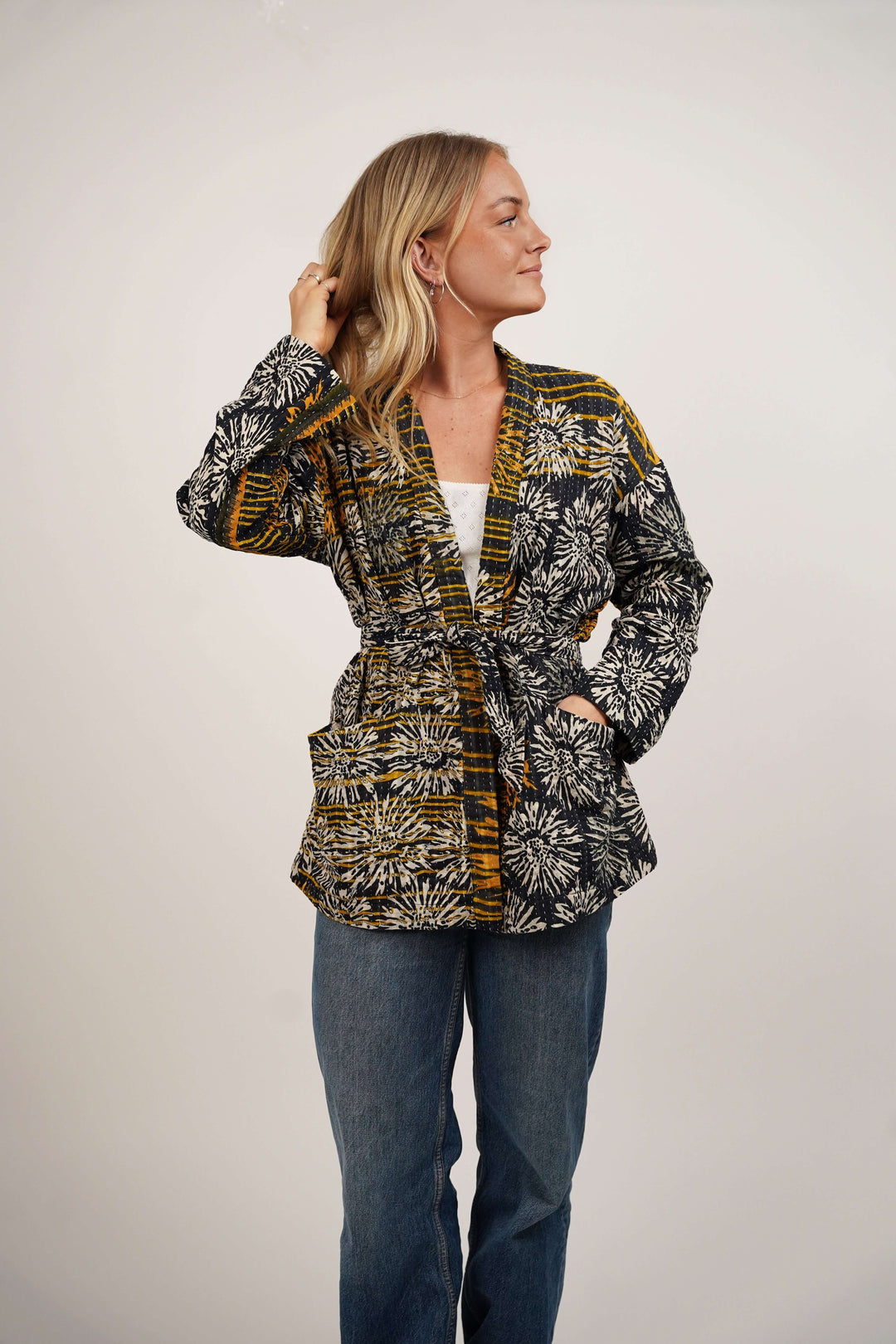 Woman wearing a patterned jacket and jeans on a plain background