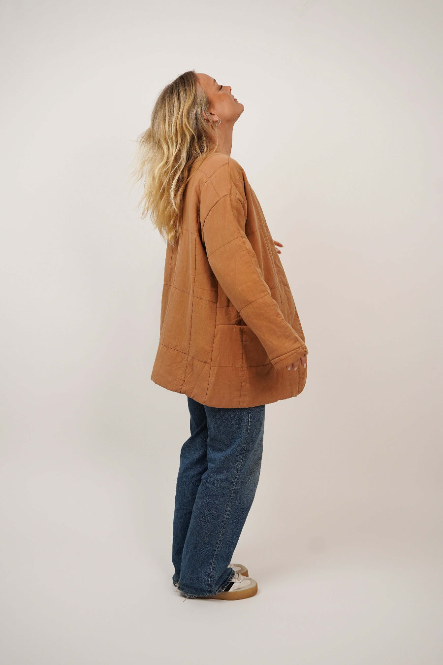 Person wearing a brown jacket and blue jeans standing against a white background