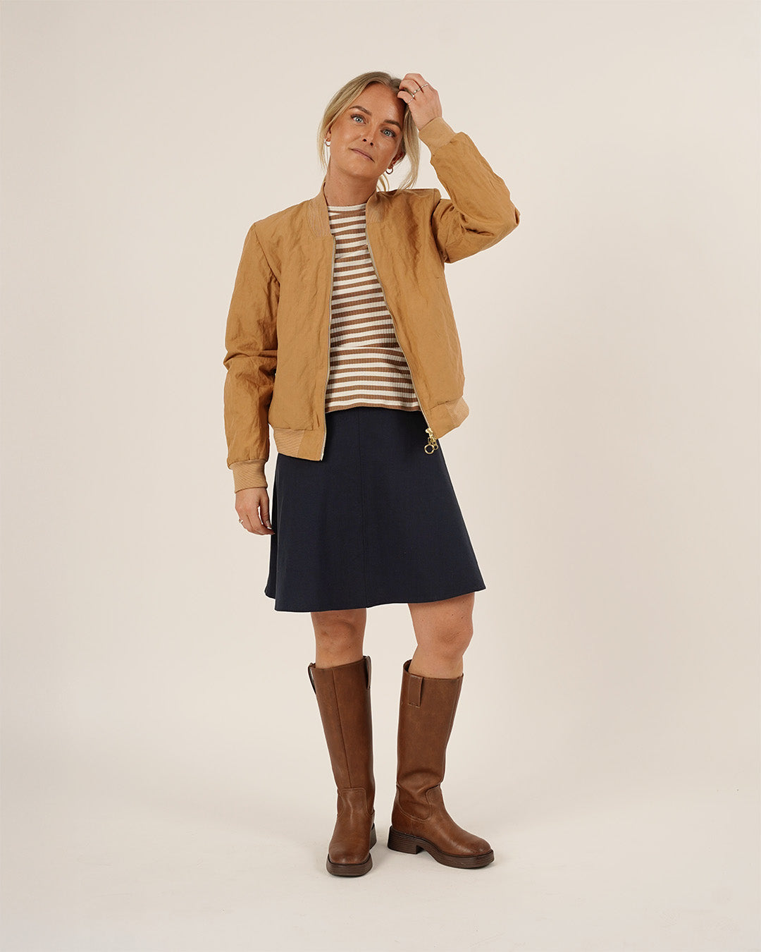 Woman wearing the Amelia Bomber Jacket sewing pattern in camel fabric layered over a striped knit top and paired with the Linea Skirt sewing pattern in navy fabric