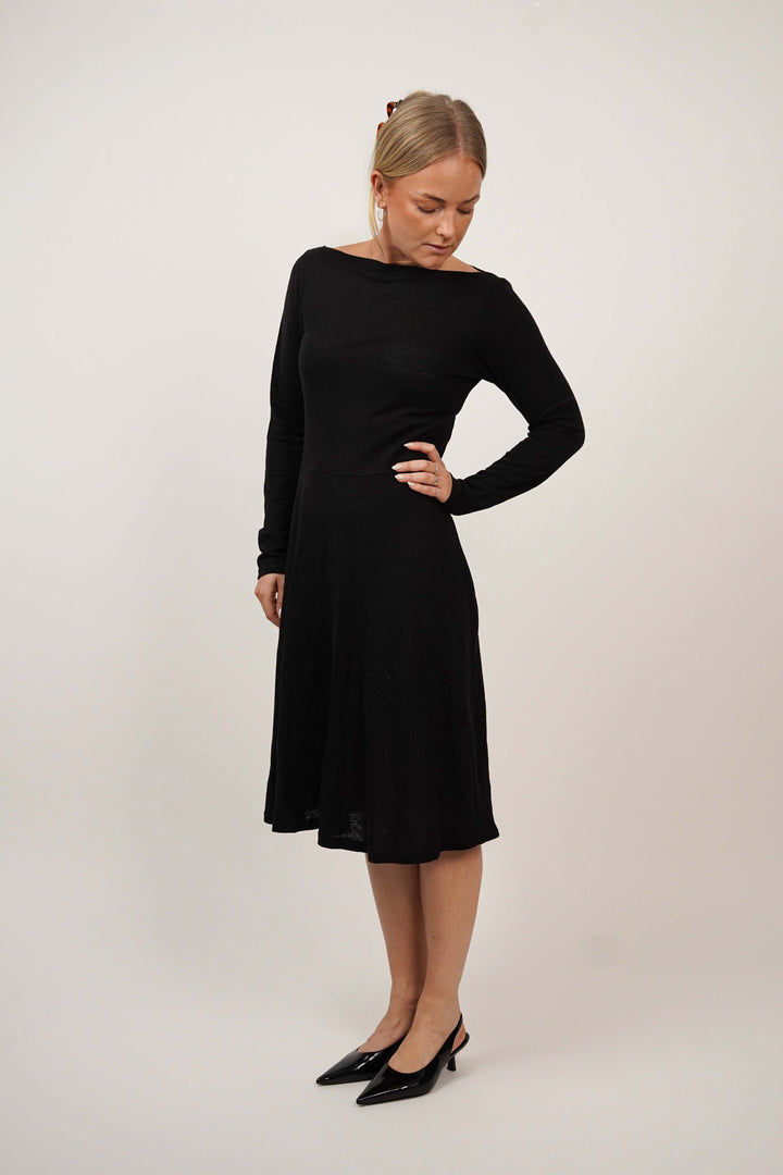 Woman wearing the Asta Dress sewing pattern in black jersey, shown from a three-quarter side angle