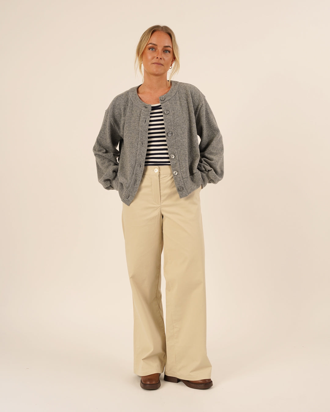 Woman wearing the Balloon Cardigan sewing pattern in grey knit fabric layered over a striped top and paired with Hepburn Pants in beige cotton twill