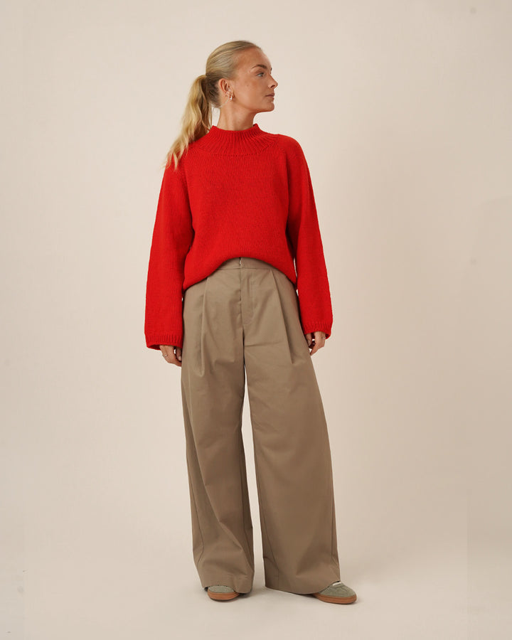 Woman wearing the Bermuda Pants sewing pattern in beige cotton twill, paired with a bright red knit sweater, shown from the front