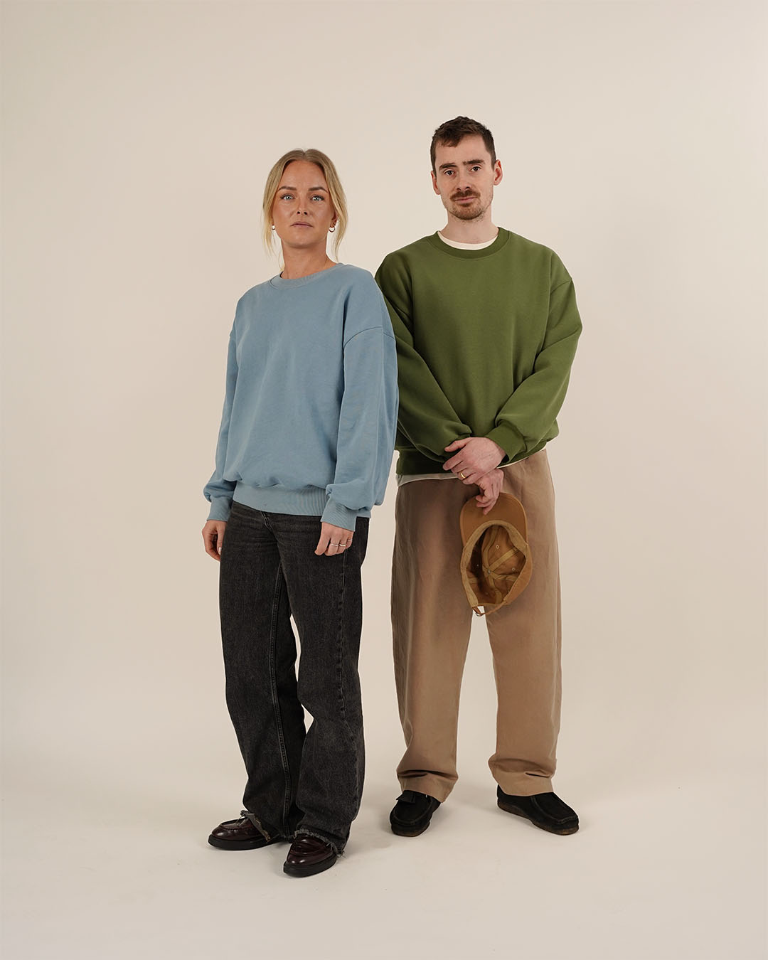 Woman and man wearing the Boyfriend Sweater sewing pattern in oversized sweatshirt fabric, shown in blue and green versions with relaxed unisex fit