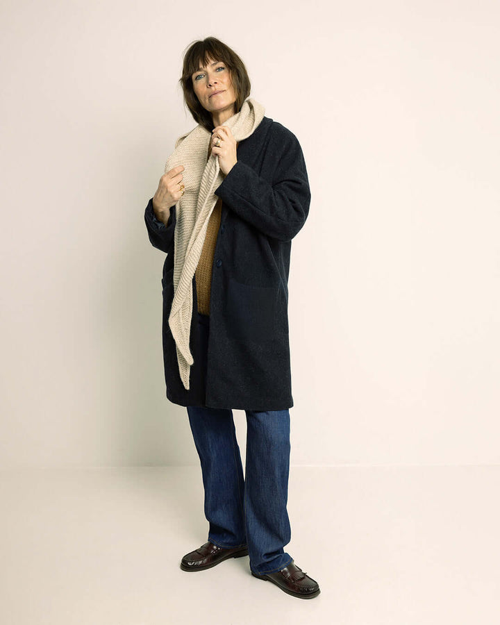 Woman wearing the Cocoon Coat sewing pattern in dark wool fabric and a scarf shown from the front with hands in pockets
