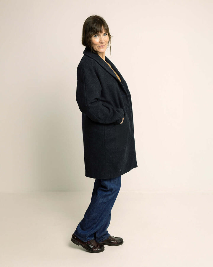 Woman wearing the Cocoon Coat sewing pattern in dark wool fabric, shown from the side with hands in pockets