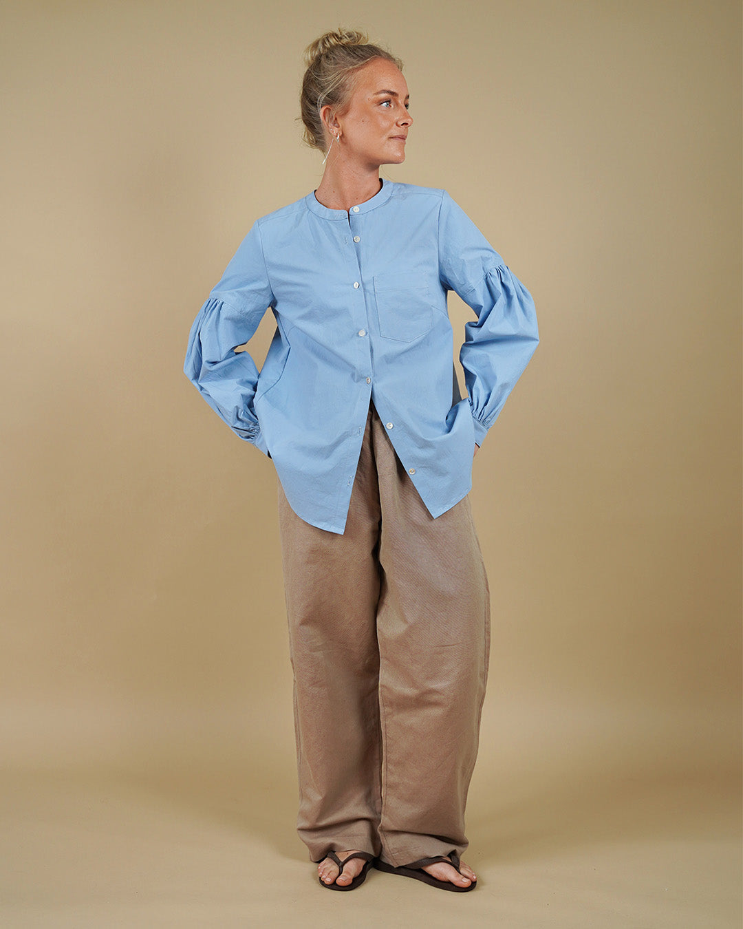 Woman wearing a collarless shirt with gathered sleeves and volume pants sewing pattern, front three-quarter view