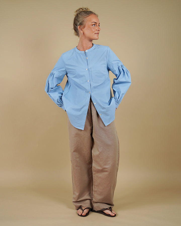 Woman wearing a collarless shirt with gathered sleeves and volume pants sewing pattern, front three-quarter view