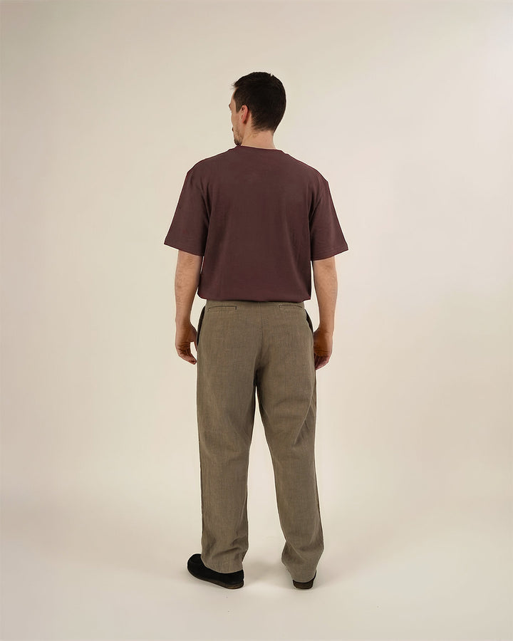 Man wearing the Men's Pleated Pants and Big T-shirt sewing patterns, shown from the back in taupe pleated trousers and a dark mauve oversized T-shirt