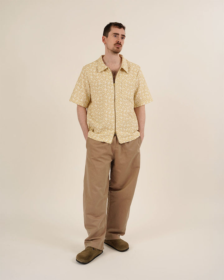 Man wearing a yellow patterned shirt and brown pants on a beige background