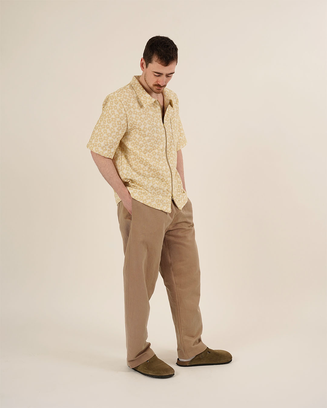 Man wearing a yellow patterned shirt and beige pants on a plain background
