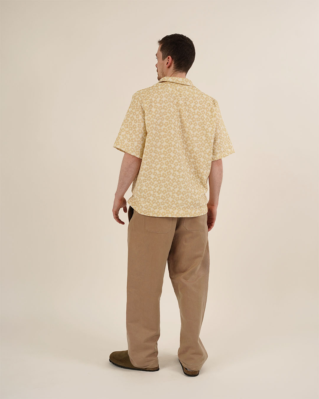 Man wearing a yellow patterned shirt and beige pants on a plain background