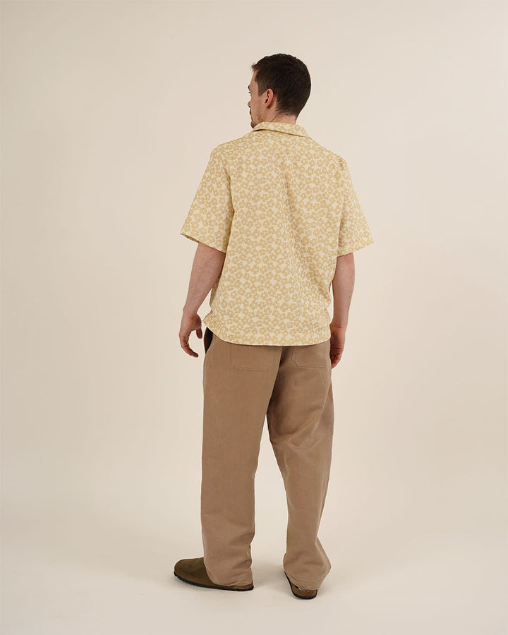 Man wearing a yellow patterned shirt and beige pants on a plain background