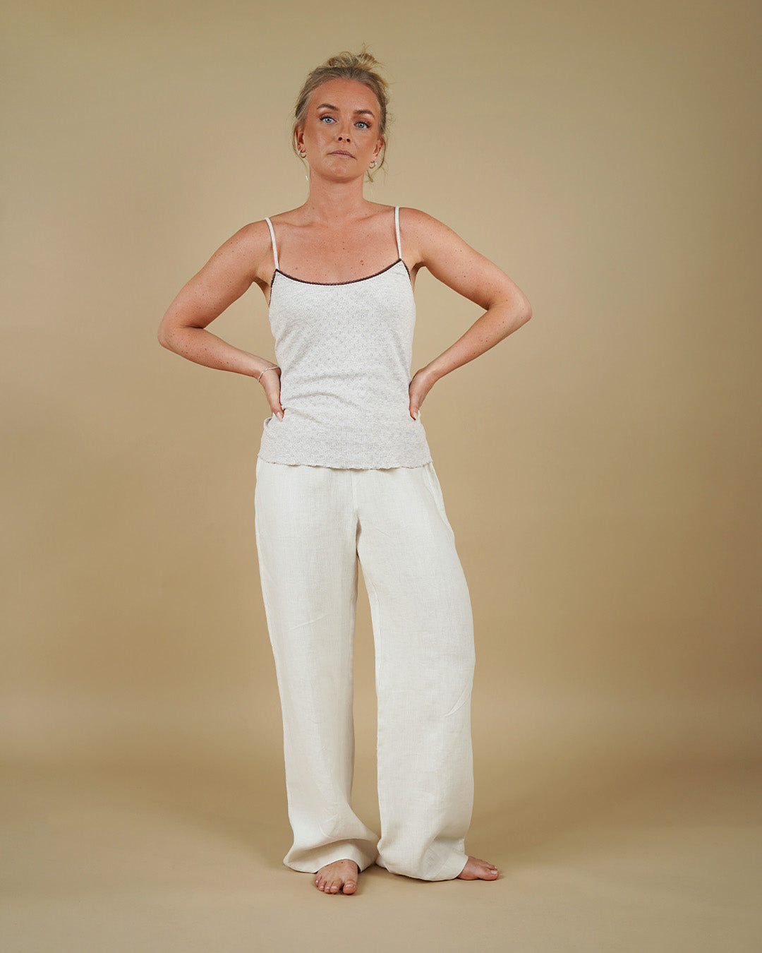 Woman wearing a white tank top and pants against a beige background